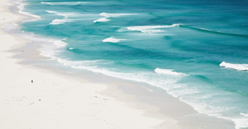A serene aerial view of turquoise ocean waves gently washing over a pristine white sandy beach.